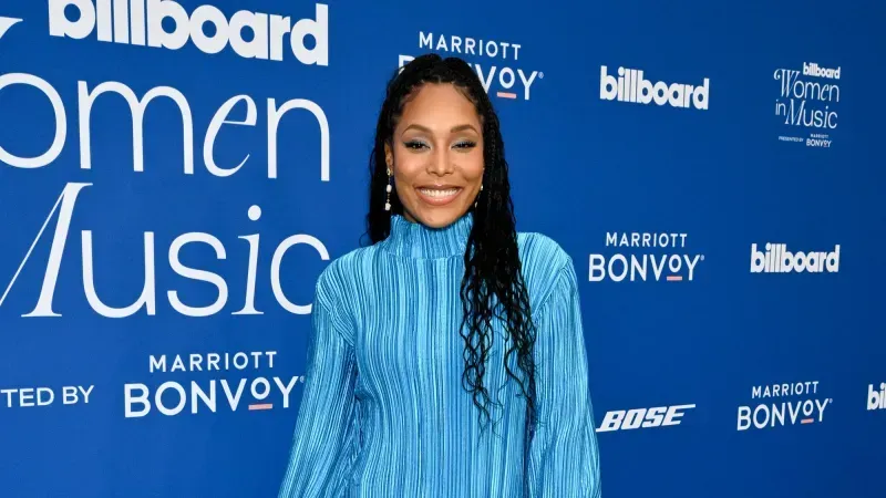 Woman in a bright blue dress smiling on a blue Billboard Women in Music red carpet backdrop.
