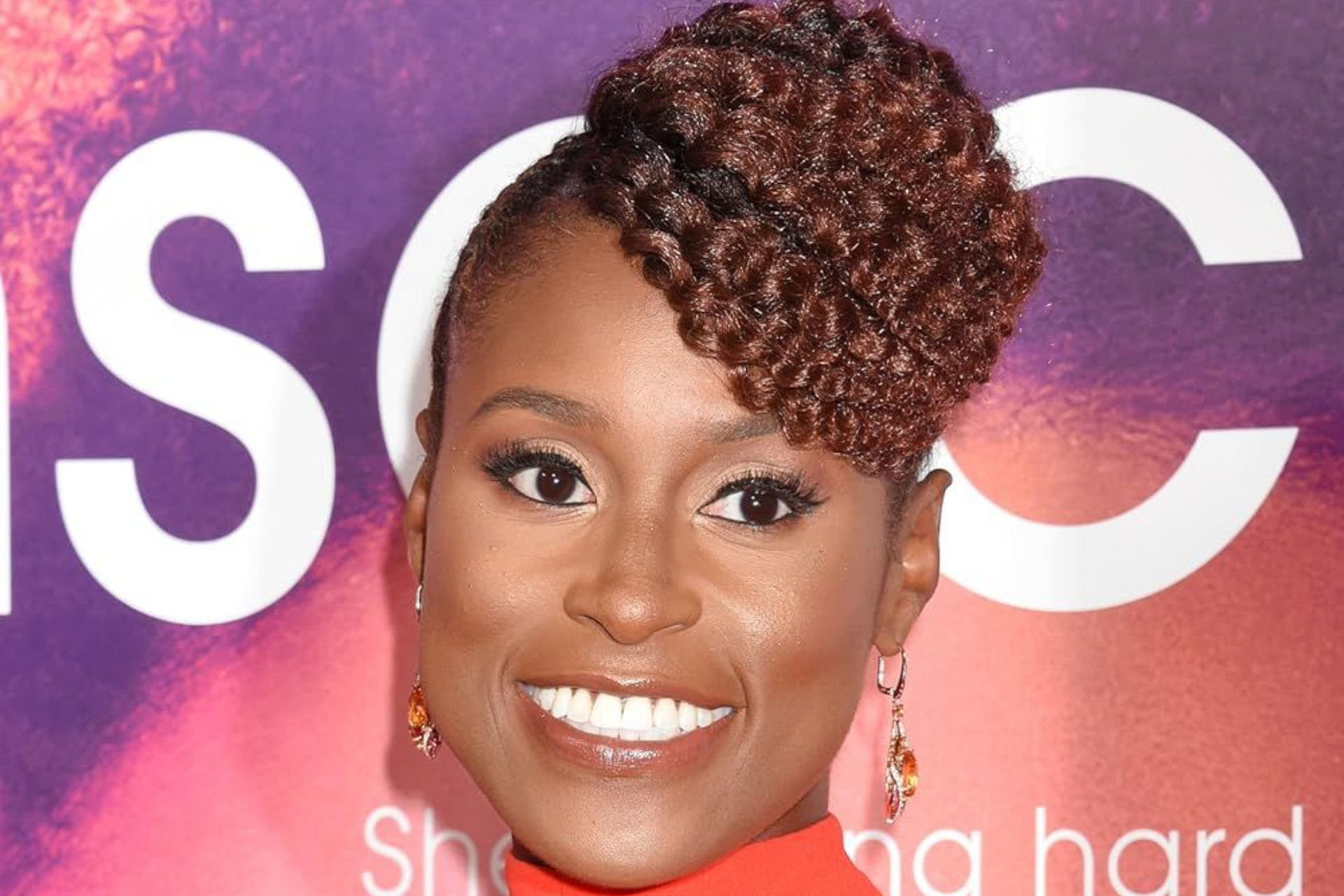 Smiling woman with braided updo in front of a purple-to-orange backdrop with large white letters