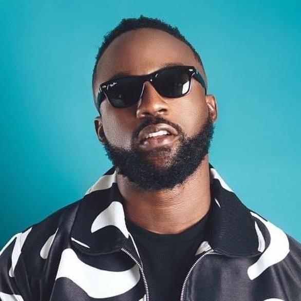 Man in black sunglasses and patterned jacket against a turquoise background.