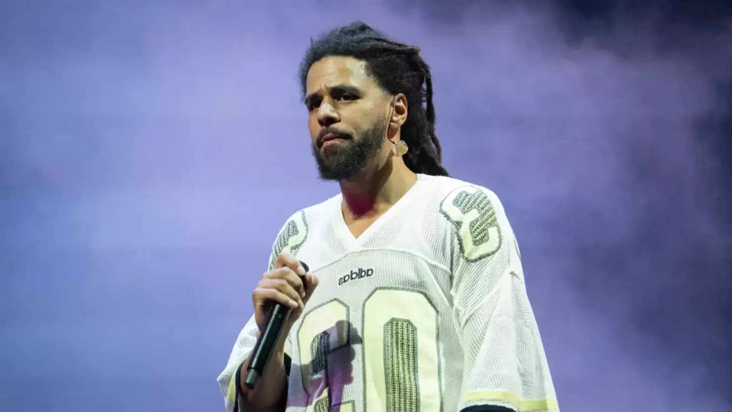 Football player in white jersey holding a microphone on a smoky purple-lit stage