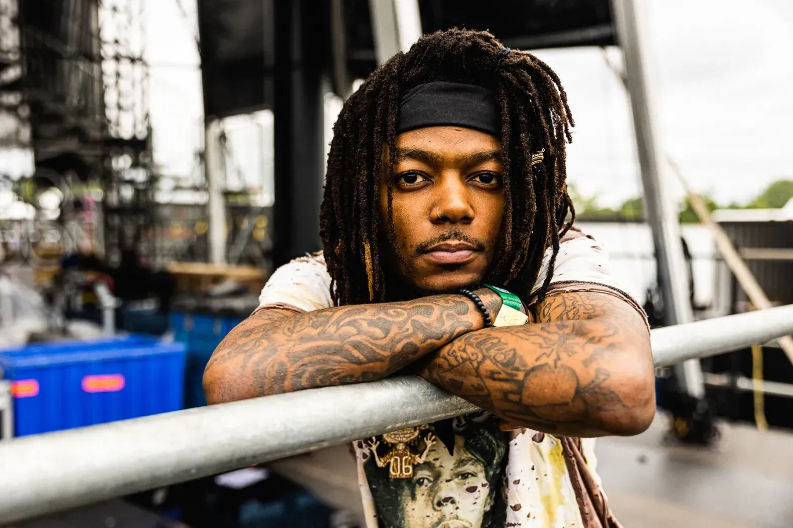 Person with dreadlocks leaning on a railing in an outdoor industrial setting