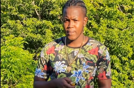 Person in a floral shirt standing outdoors in front of lush green foliage, looking at the camera.