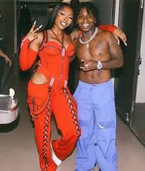 Two people smiling and posing indoors, one in a red outfit and the other in blue pants