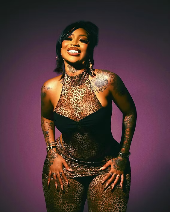 Smiling person in a glittery black dress posing against a purple backdrop