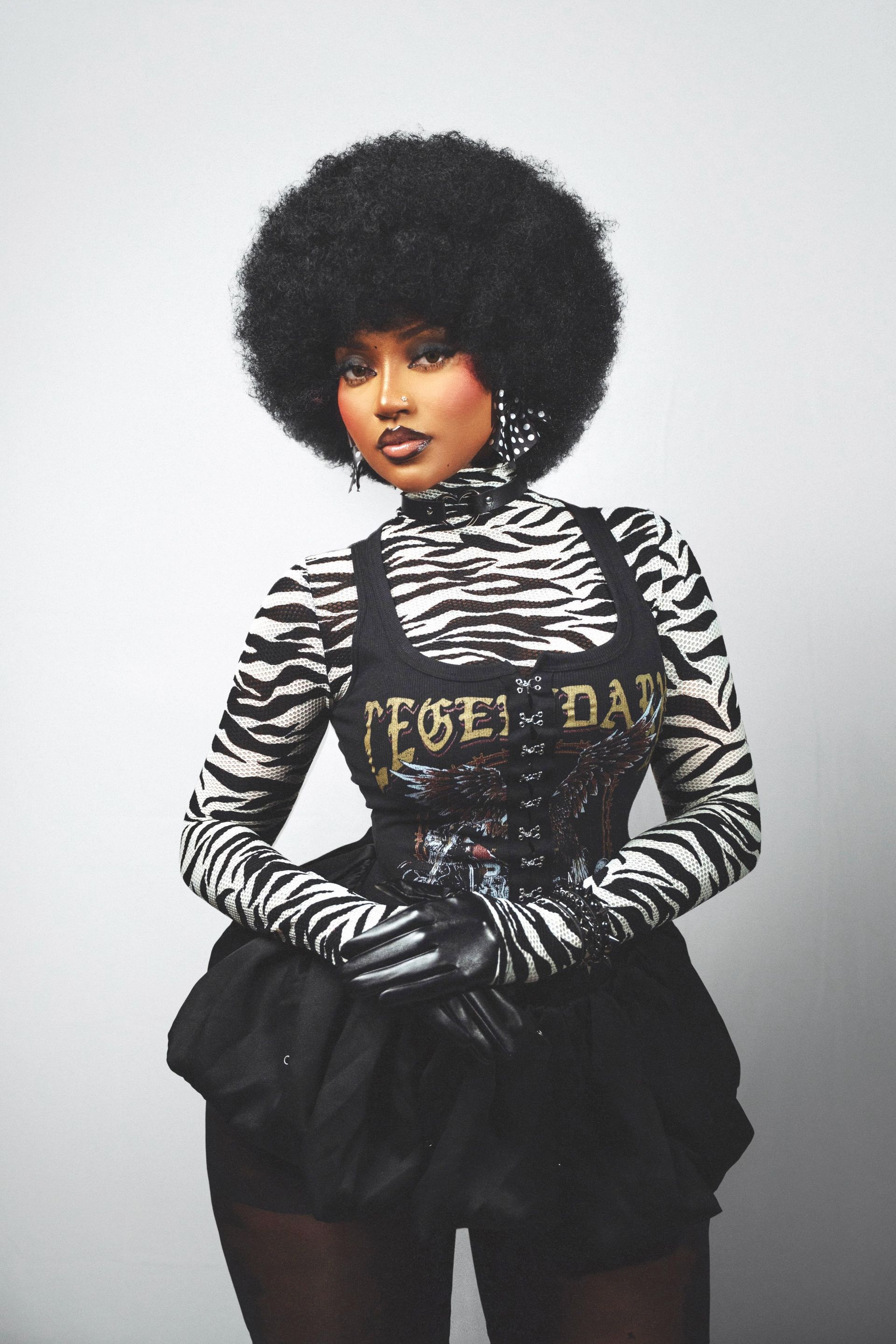 Person in zebra-striped top, black shorts, and gloves, posing against a plain light background.