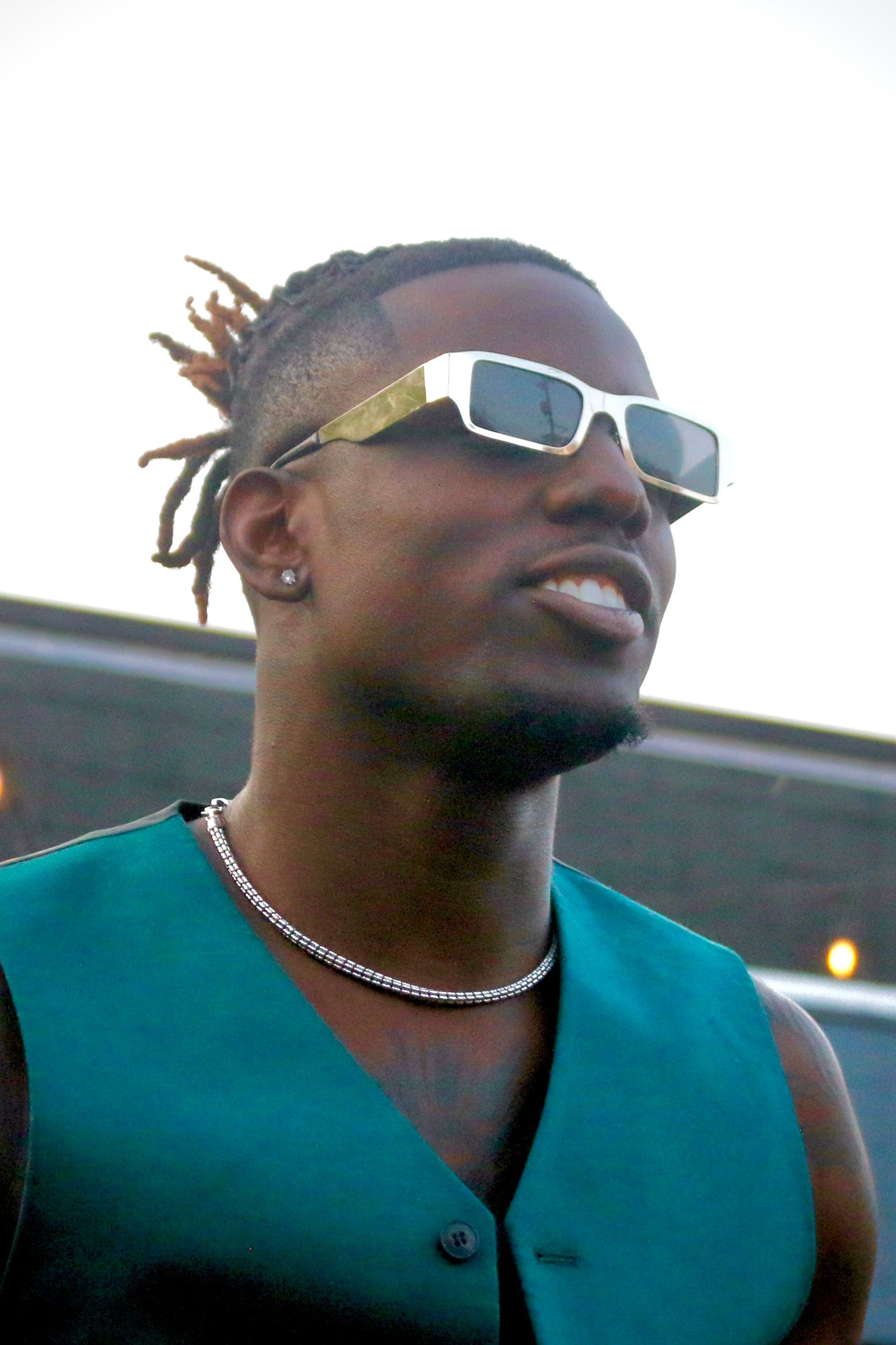 Smiling man in sunglasses and teal vest outdoors, looking to the side.