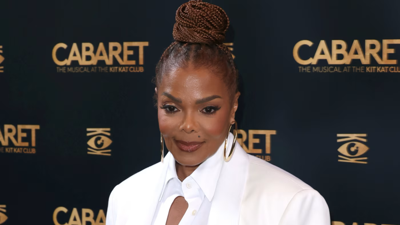 Woman in a white blazer at a Cabaret event backdrop, wearing a braided updo and gold earrings