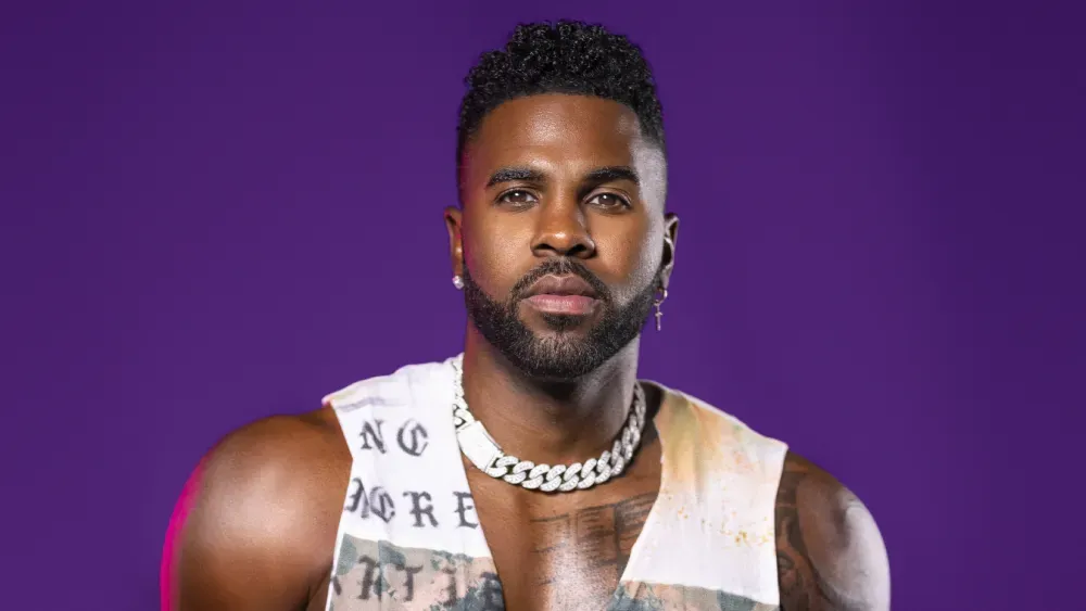 Portrait of a man with a beard and chain necklace against a purple background, facing forward