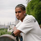 Person leaning on a railing outdoors, wearing a white shirt, with a city skyline in the background