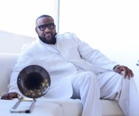 Man in white suit reclining on white couch beside a large brass horn-shaped speaker