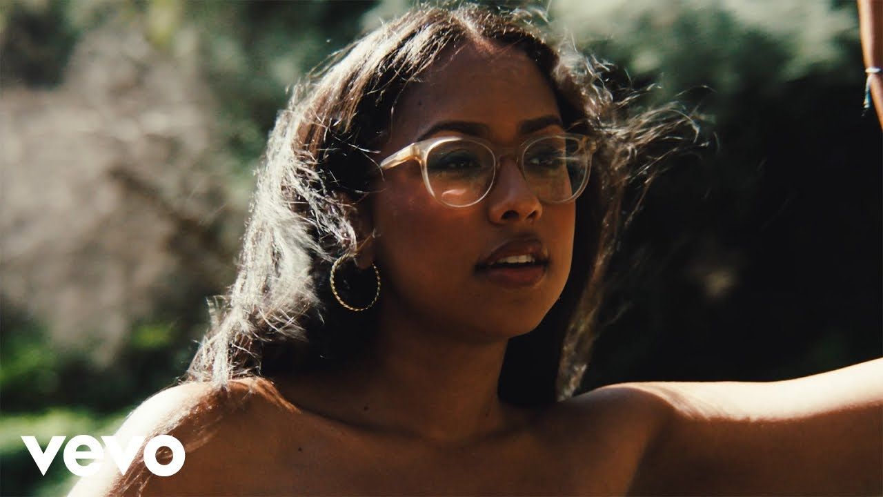 Woman wearing glasses outdoors, arm raised in bright sunlight, with a VEVO logo in the corner