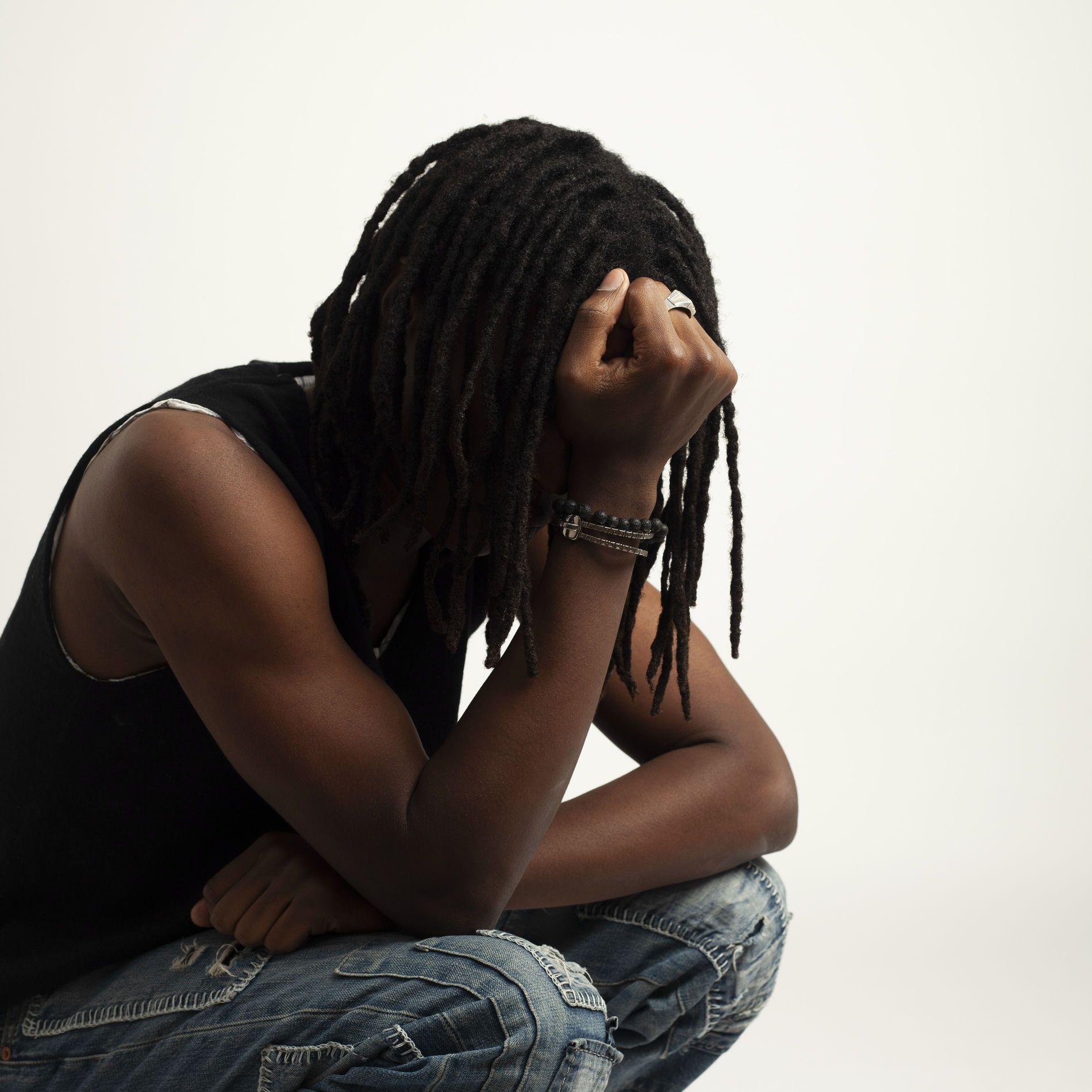 Person sitting with head in hand, looking down in a white studio background