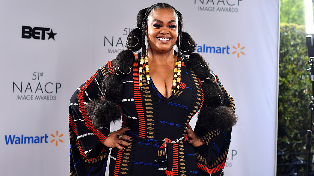 Woman smiling on a red carpet at a NAACP event, wearing a black and red dress.
