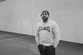 Man standing on a court in an Illinois sweatshirt, hands in pockets, smiling at the camera.