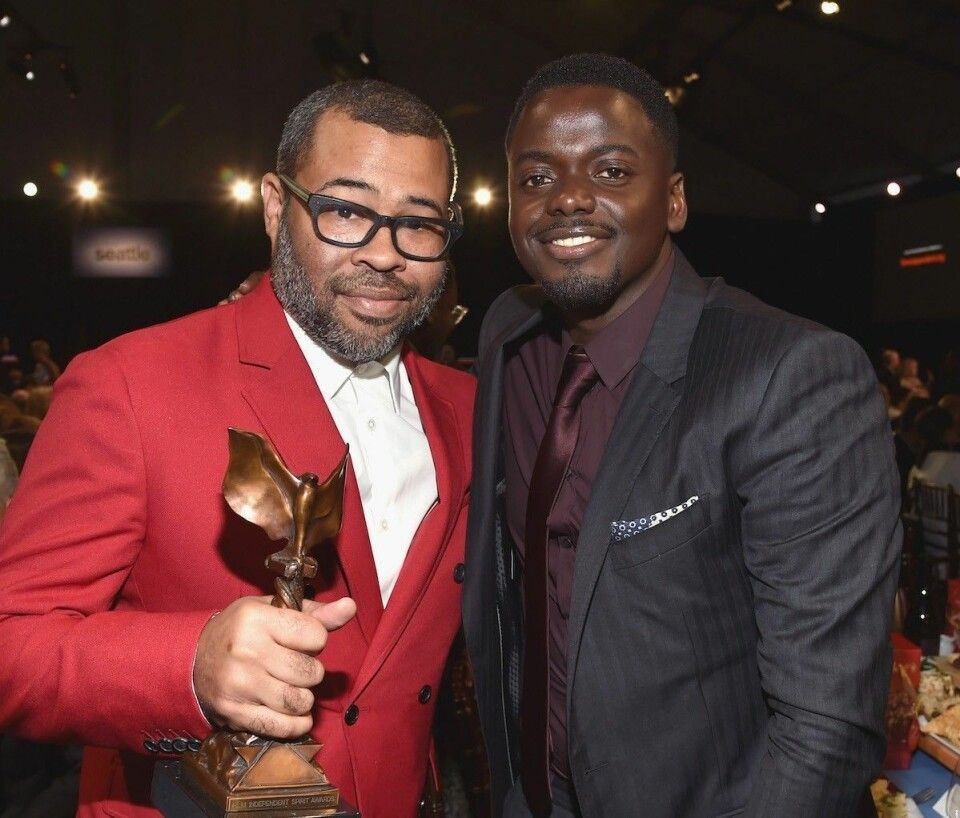 Two men in suits smiling at an awards event, one holding a trophy in a dimly lit venue.
