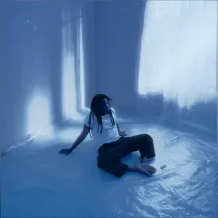 Person seated on a blue-lit floor in a sparse room, leaning back against the wall.