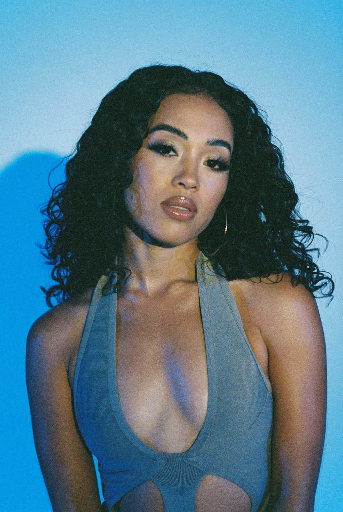 Woman with curly dark hair in a blue halter top against a blue background