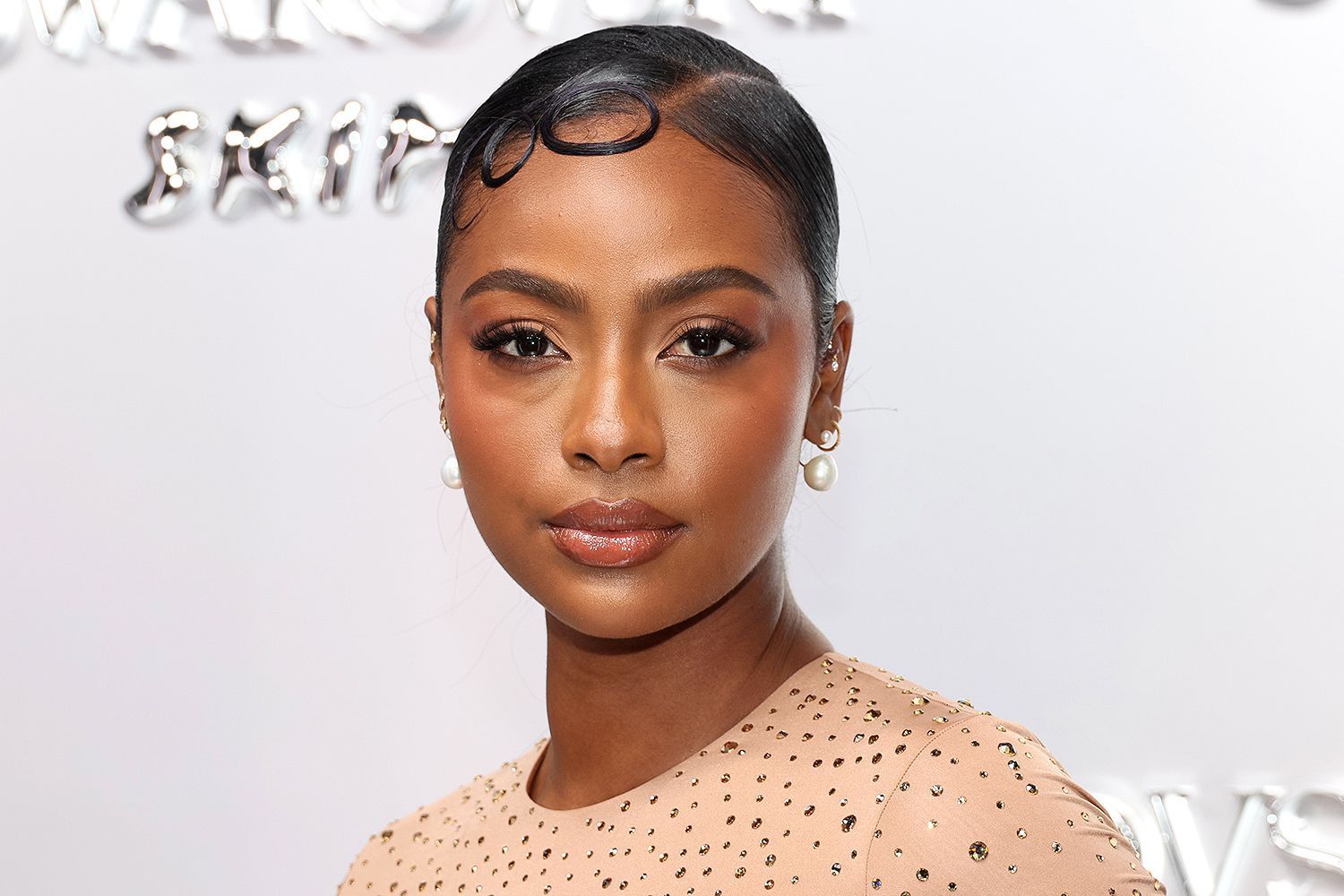 Portrait of a woman with a sleek updo and soft makeup, wearing a blush beaded dress on a red carpet