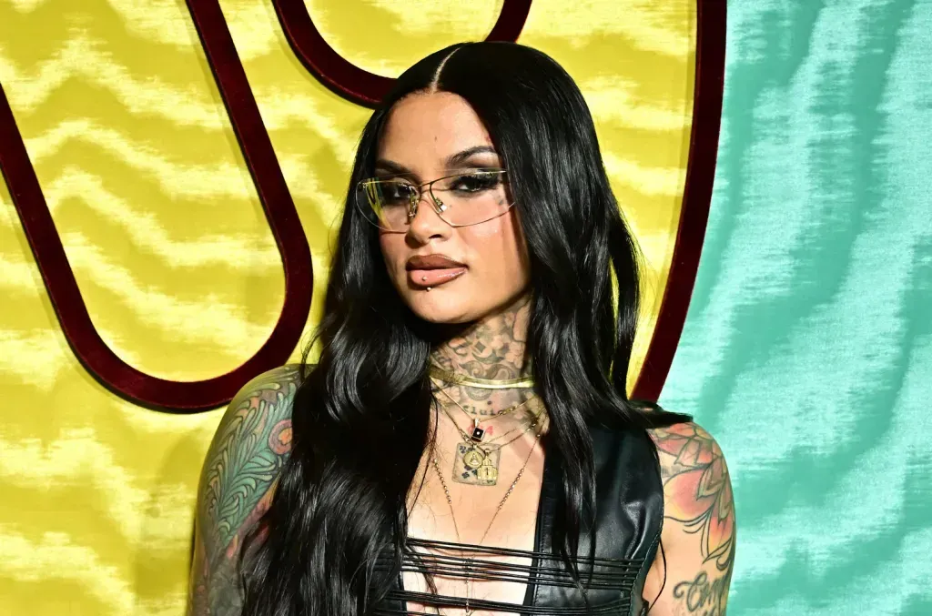 Woman with long black hair and tattoos posing at a colorful event backdrop