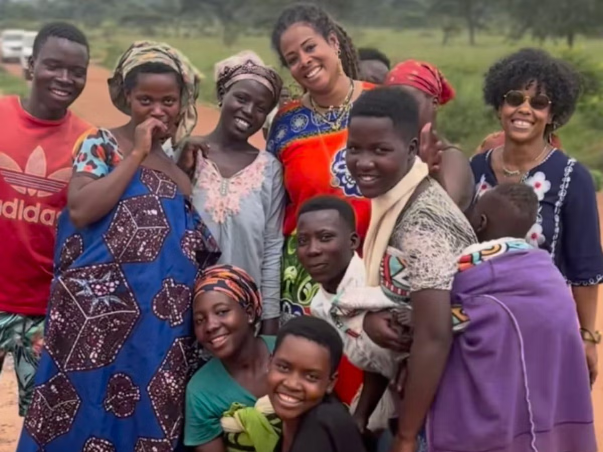 Group of smiling people posing outdoors, with colorful clothing and a purple bag in front