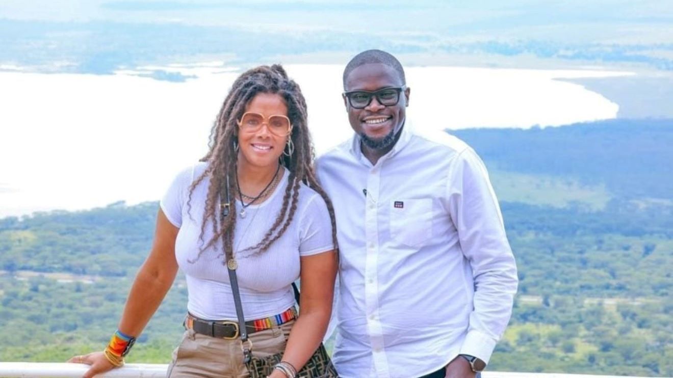 Two people smiling on a scenic overlook with a lake and forest in the background
