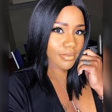 Woman with straight black hair, wearing a black top, posing indoors and resting her hand on her face