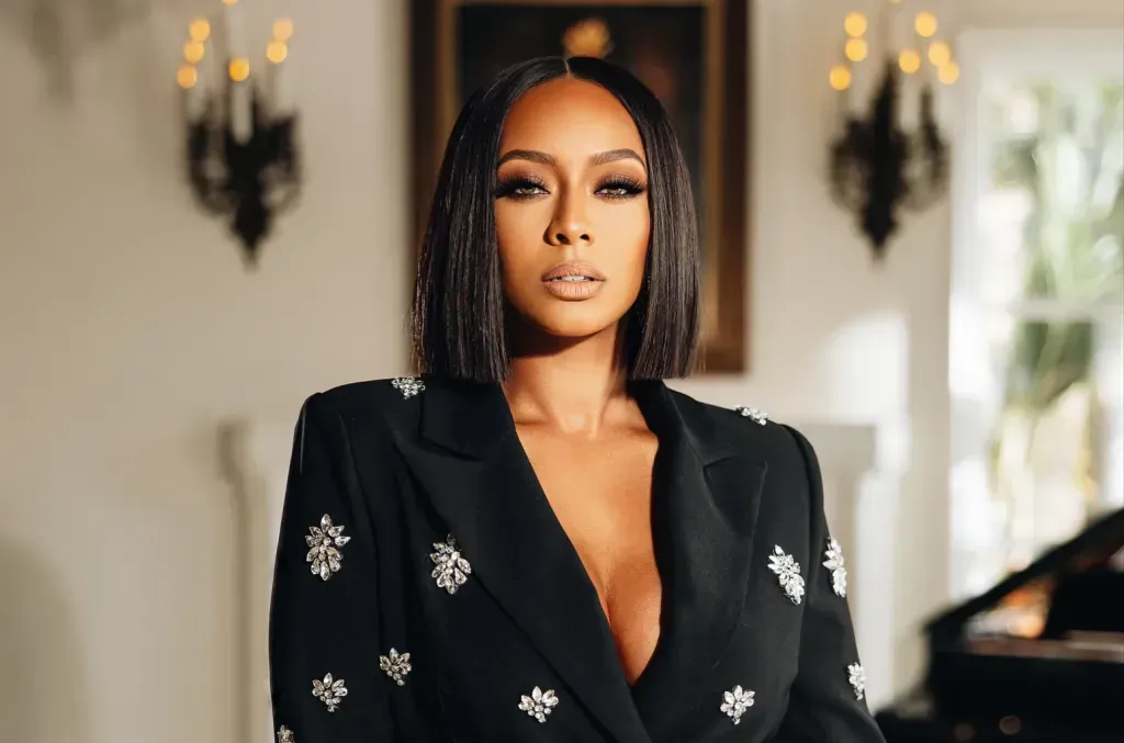 Woman in a black blazer with silver embellishments, standing indoors against a softly lit background