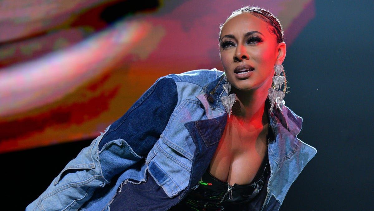Singer onstage in a blue denim jacket, leaning under red and purple concert lights.