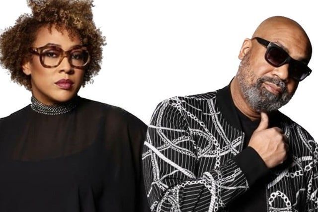 Two stylish adults posing against a white background, one in glasses and black top, one in sunglasses and patterned jacket