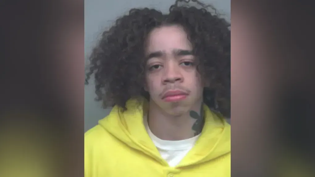 A person with curly hair and a yellow hoodie facing the camera against a plain background