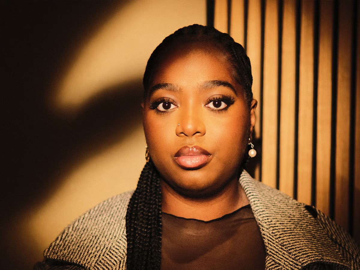 Portrait of a person in warm light, wearing a textured shawl against a striped background.