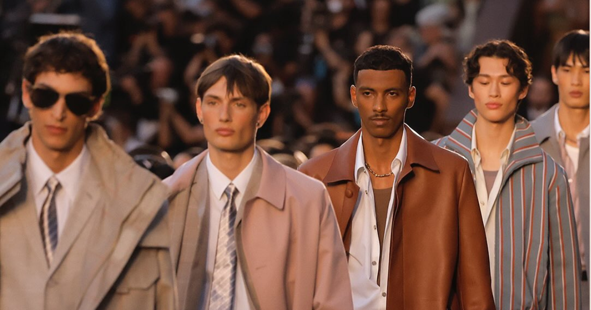 Male models walking a runway in tailored neutral-toned outfits at a fashion show