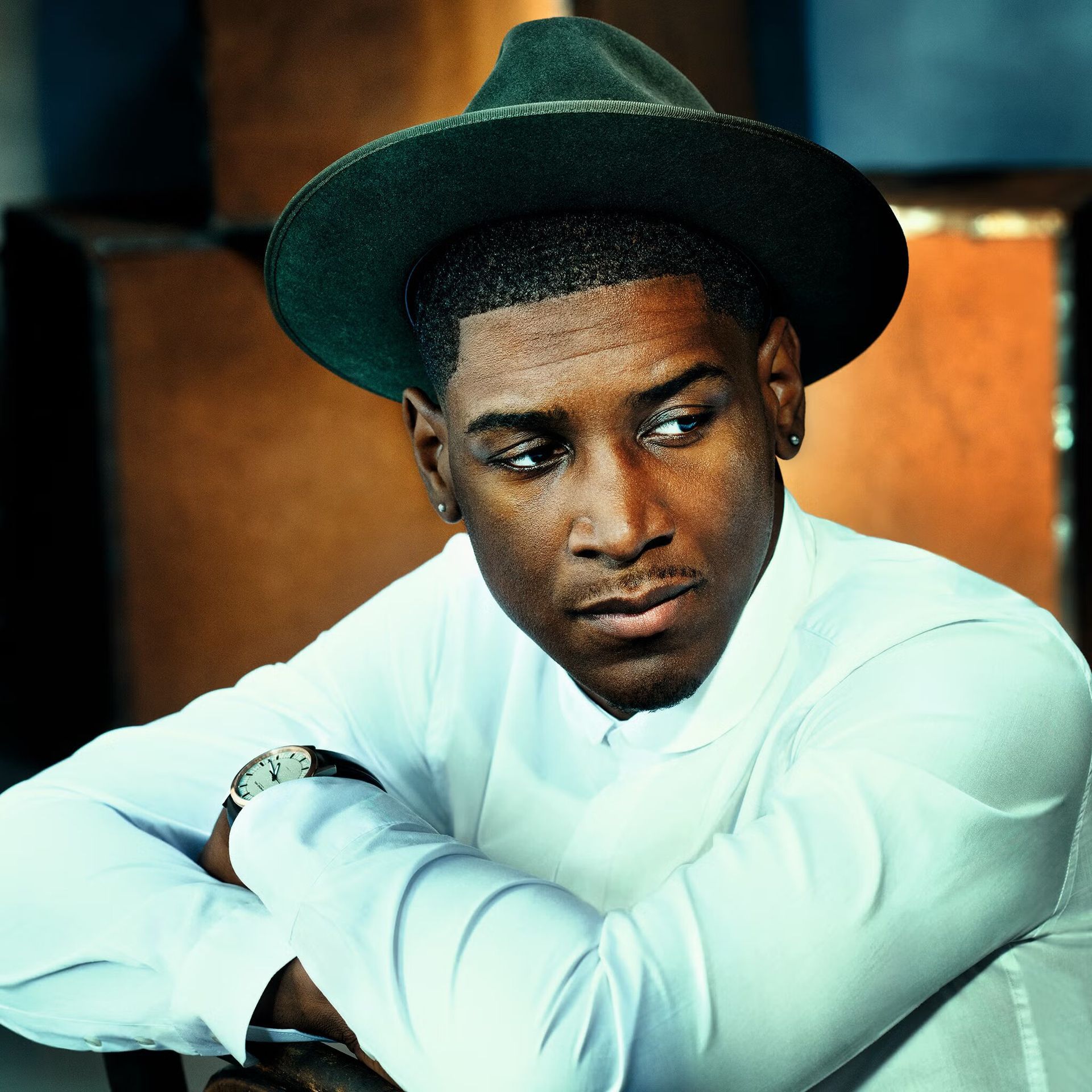 Young man in a white shirt and dark hat, leaning on his arms with a thoughtful expression.