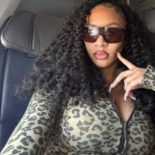 Woman in sunglasses and leopard print top posing in a car seat with hand near her face