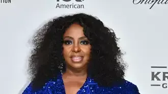 Woman in a blue sequined jacket posing at a step-and-repeat event backdrop.
