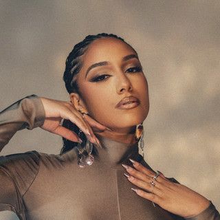 Portrait of a person with braided hair posing in a sheer brown top against a warm beige backdrop