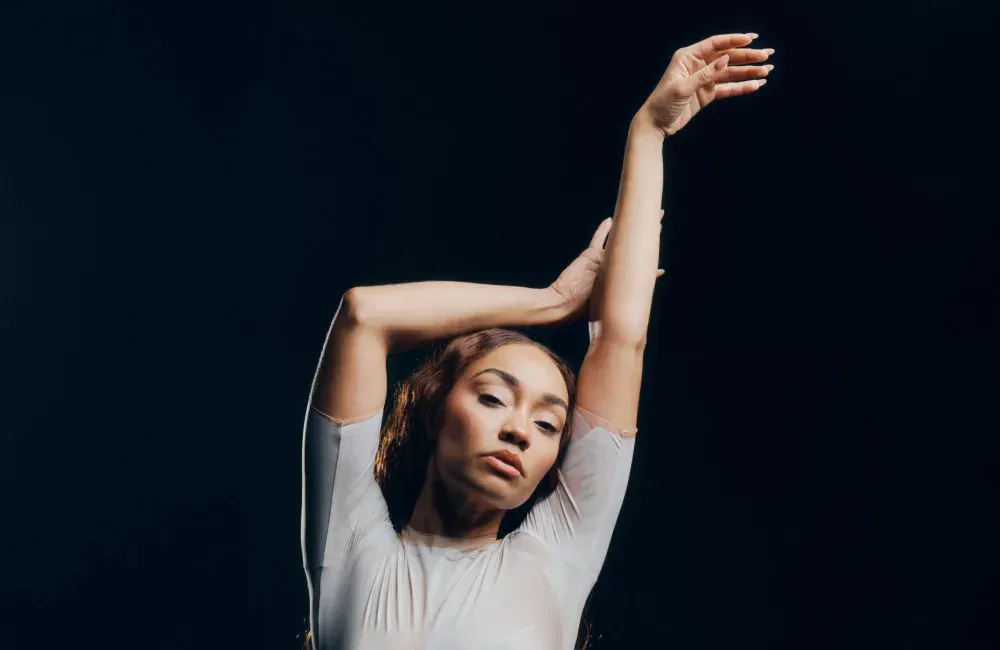 Person in a white shirt posing with arms raised against a dark background
