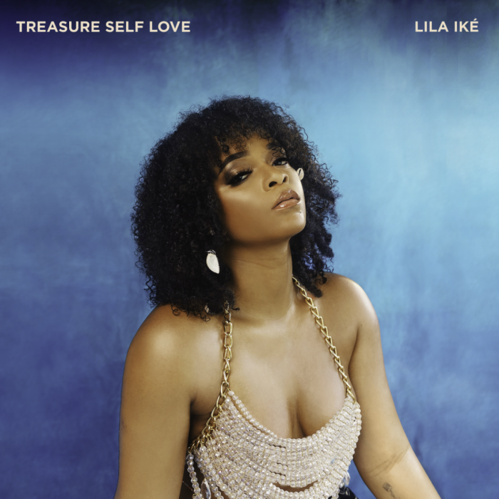 Woman with curly hair in a beaded dress against a blue studio backdrop, titled “Treasure Self Love.”