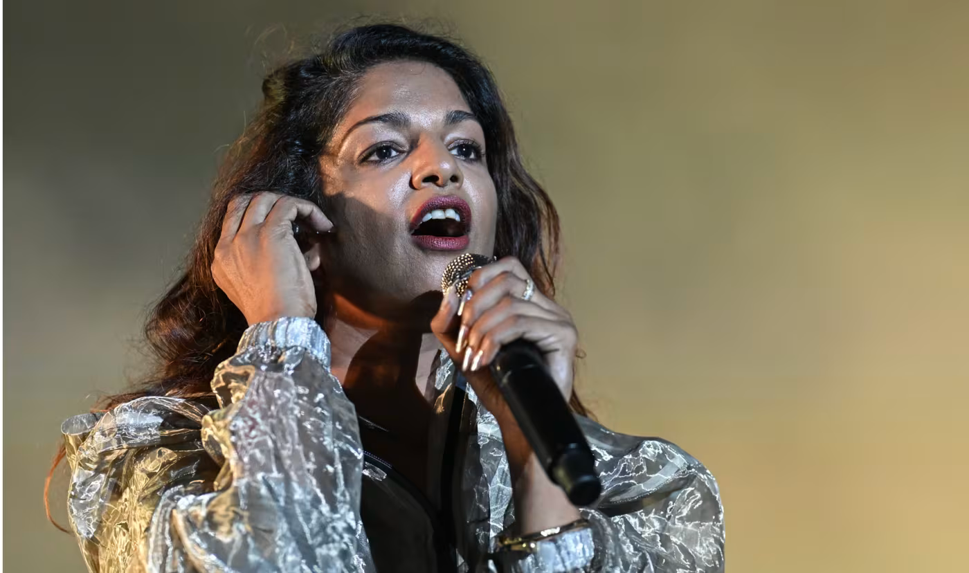 Singer performing on stage with microphone, wearing a shimmering silver outfit and singing passionately.