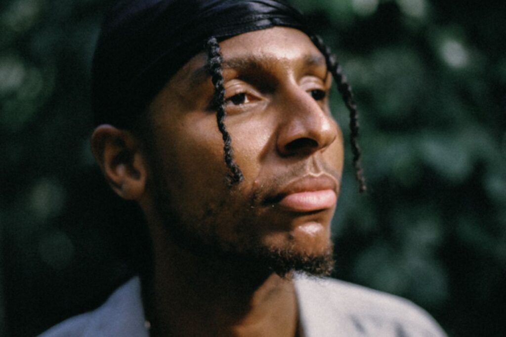Close-up of a person in a black headscarf, looking to the side against a blurred green background
