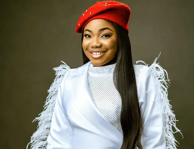 Smiling person in a red beret and white fringed outfit against a gray background