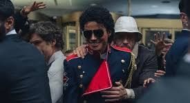 Man in a dark military-style jacket and red scarf moves through a crowded indoor venue while people cheer nearby