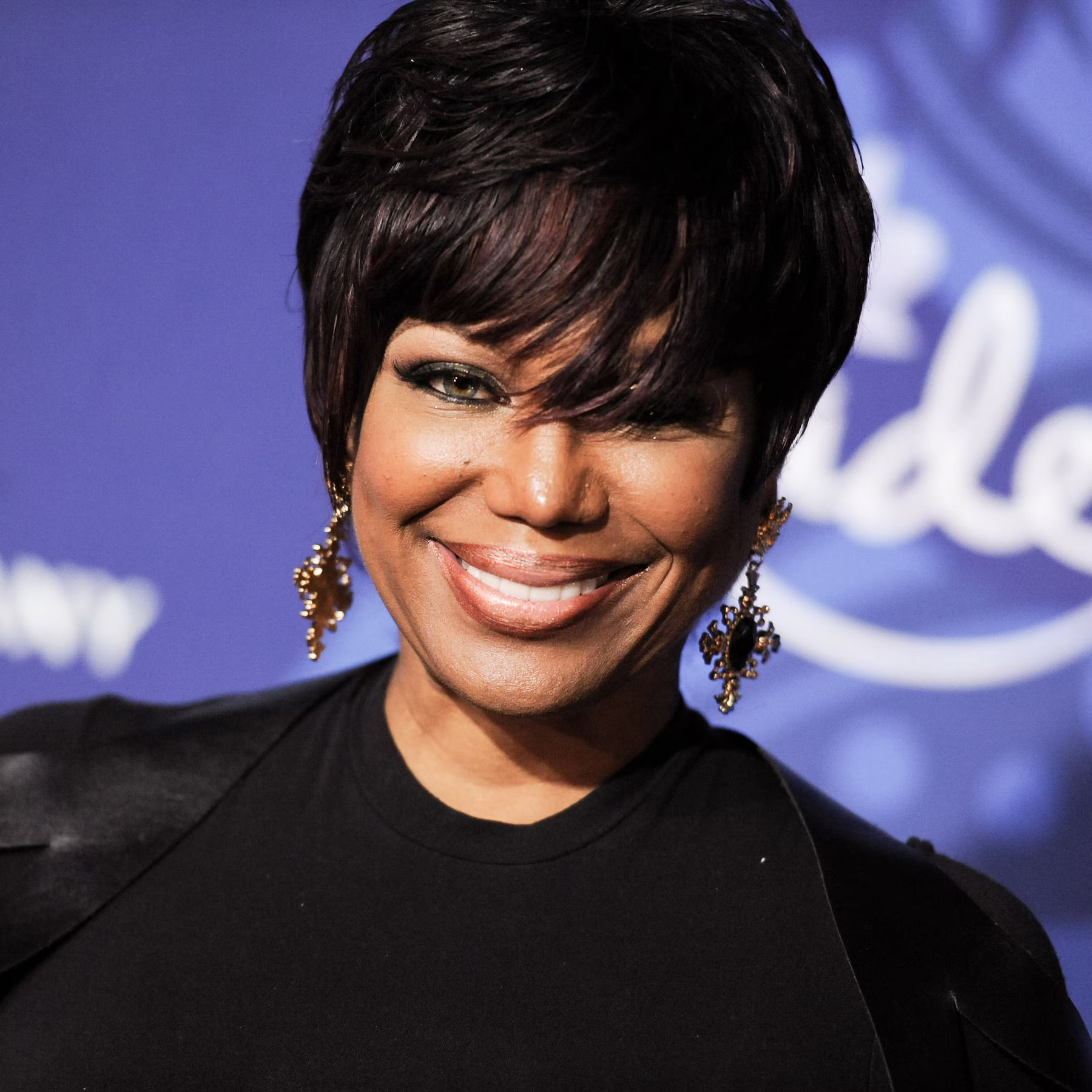 Smiling woman with short dark hair in a black top at a blue event backdrop
