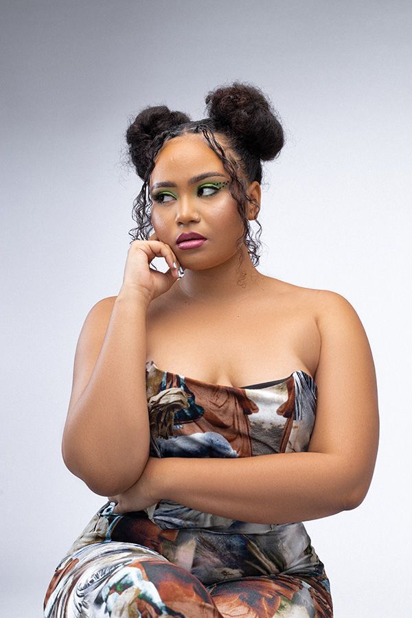 Woman in a strapless patterned dress posing thoughtfully against a light gray backdrop