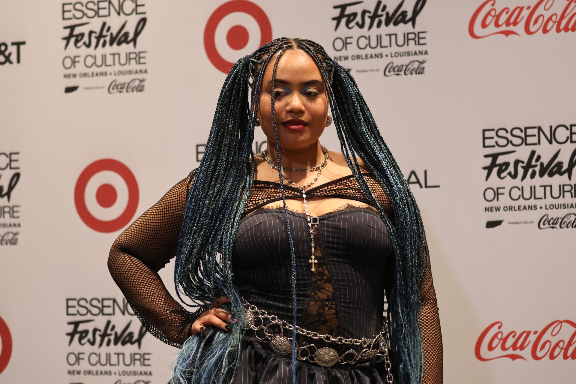 Woman with blue braids posing on a red carpet at the Essence Festival of Culture backdrop