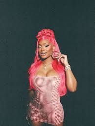 Person with long pink hair and a pink checkered outfit posing against a dark background.