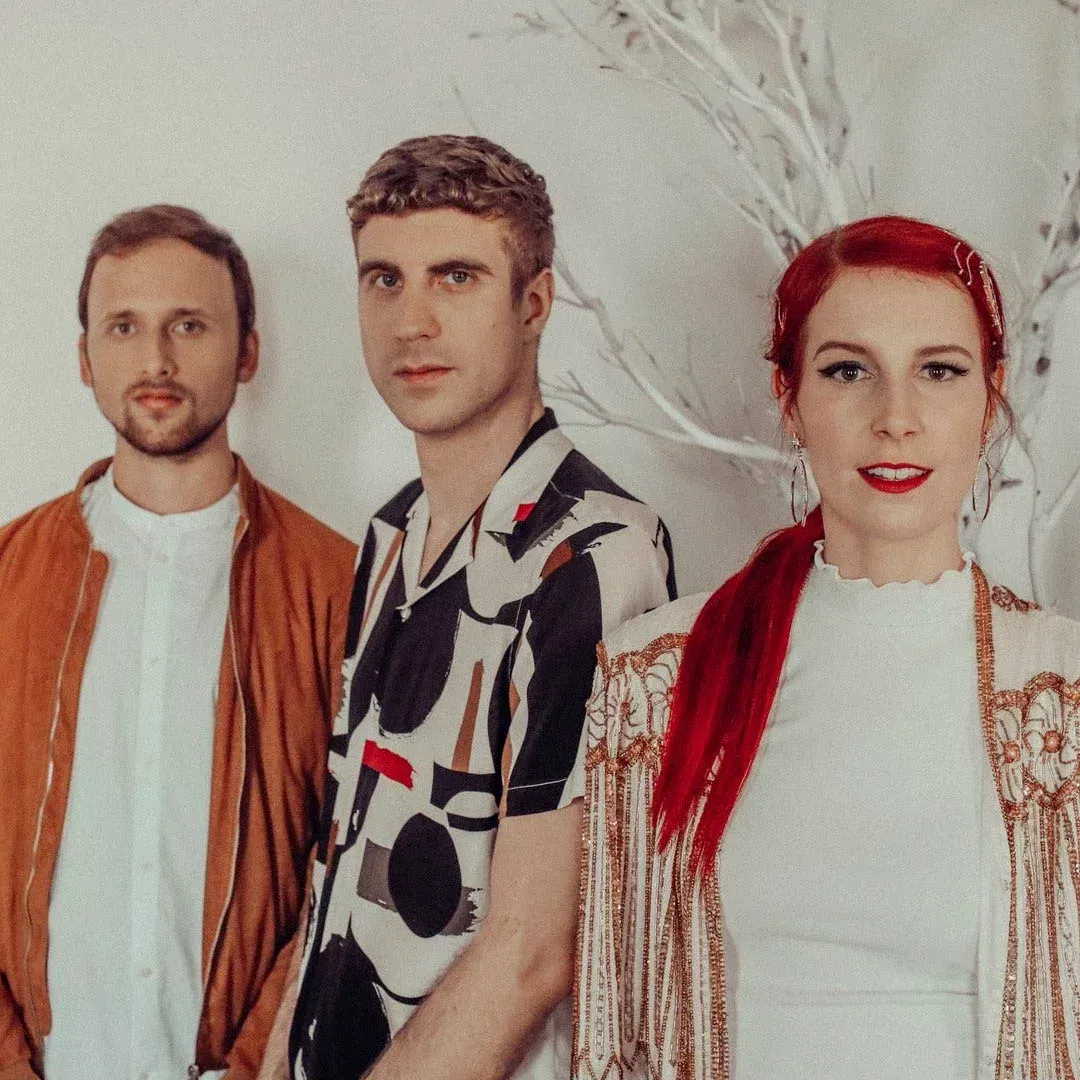 Three people posing against a light wall, wearing colorful casual outfits.