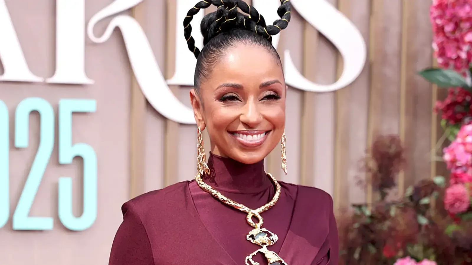 Smiling woman in a burgundy dress on a pink carpet with floral decor