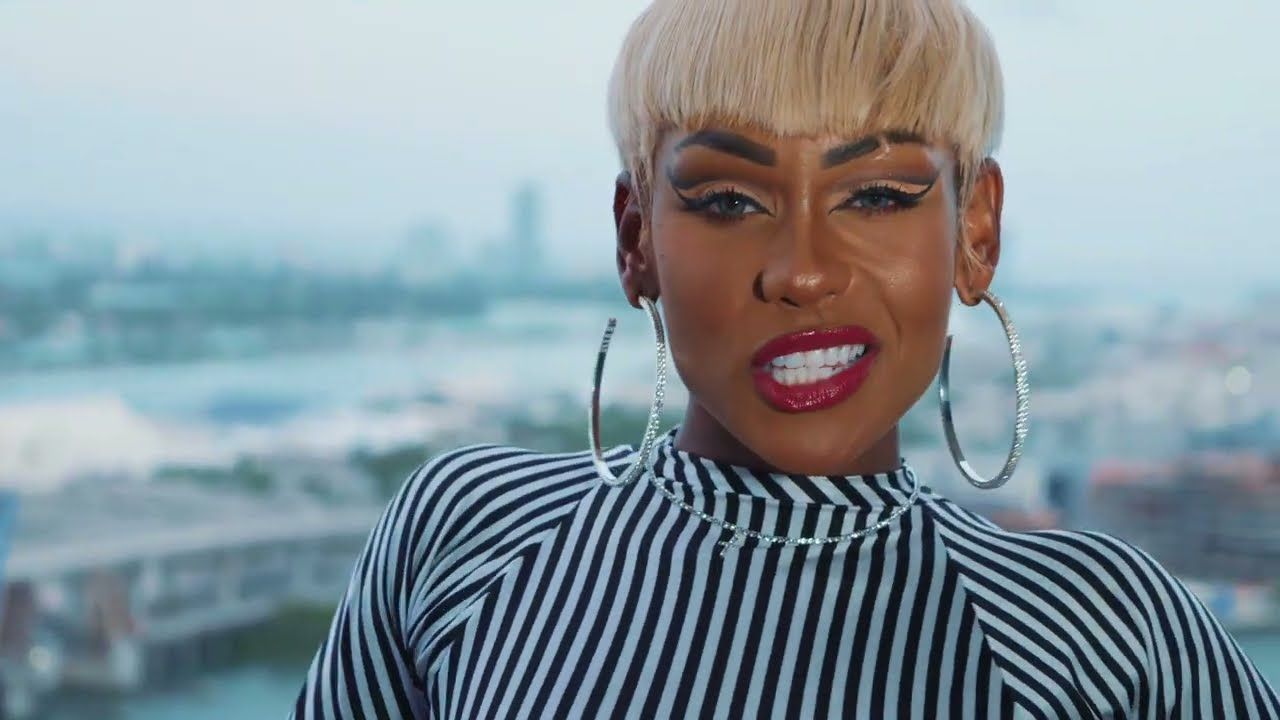 Person with blonde hair and hoop earrings singing outdoors, wearing a black-and-white striped top.