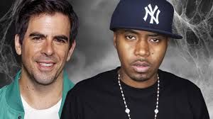 Two men in front of a smoky gray background, one wearing a Yankees cap and black shirt.
